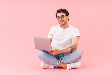 Image of cheerful man using laptop while sitting with legs crossed