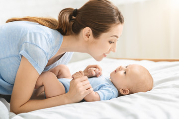 Young mother playing with her cute little baby in bed