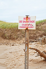 An old sign in French, translated into English as 'life preserver, for emergency use only' and with several bullet holes in it, can be found on a beach in Canada's Madeleine Islands.