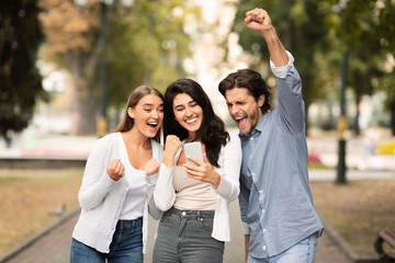 Three friends reading great message on cell phone in park
