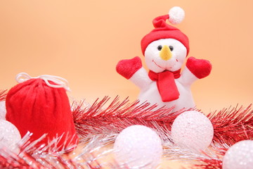 Christmas background. Toy snowman and a red bag with gifts among tinsel and Christmas balls.