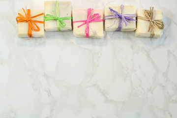 handmade organic soap in gift wax wrapping  paper with multi colored eco raffia ribbons on marble surface with space for text. Instagram style soap flat lay frame