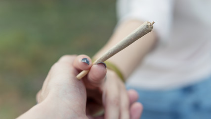 Close-up of females hands holding marijuana joint, smoking cannabis blunt outdoors. - obrazy, fototapety, plakaty