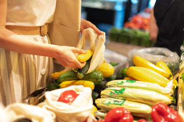 Woman chooses fruits and vegetables at farmers market. Zero waste, plastic free concept. Sustainable lifestyle. Reusable cotton and mesh eco bags for shopping.