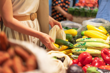 Zero waste, plastic free concept. Sustainable lifestyle. Woman chooses fruits and vegetables at farmers market. Reusable cotton and mesh eco bags for shopping.