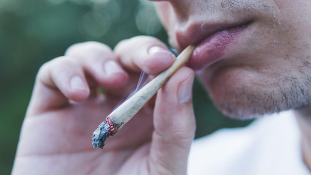 The young person smoking medical marijuana joint outdoors. The young man smoke cannabis blunt, close-up.