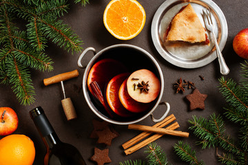 Metal pot of mulled wine on the brown table, piece of apple pie on the plate