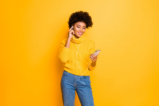Photo of nice charming cutly wavy cute pleased fascinating black girl listening to music with her headphones while wearing jeans denim pullover isolated over vivid color background
