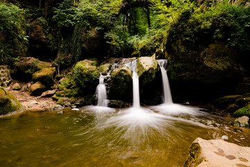 idyllic small waterfall in lush green forest landscape