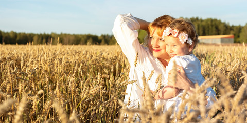 A red-haired girl and a child are standing in a field with ears of corn. Rural landscape. Family with a child, blond European girl with wavy hair. Watching the sunset