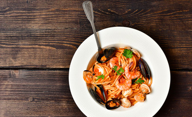 Spaghetti seafood pasta with clams and prawns with mussels and tomatoes in a white plate with on a wooden table. Recipe of Italian cuisine