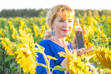 Girl with red, wavy hair. Holds a glass bottle of vegetable oil. Field of sunflowers