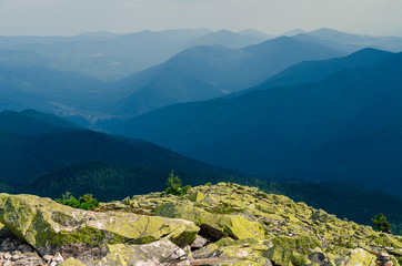 Huge stones covered with green lichen lie on the top of the mountain against the backdrop of ancient, high mountain ranges