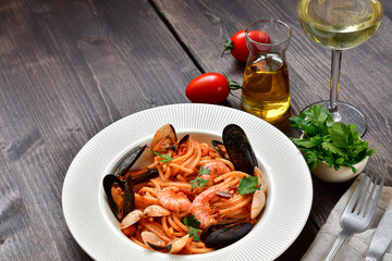 Spaghetti seafood pasta with clams and prawns with mussels and tomatoes in a white plate with on a wooden table. Recipe of Italian cuisine