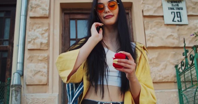 Nice mood pretty trendy girl with charming smile wearing airpods listening music going out walking on the street.