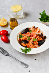 Pasta spaghetti with seafood mussels, shrimps, parsley.  In a white plate on a gray stone table, top view. Pasta recipe , Italy 