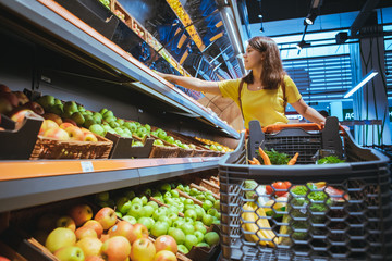 woman taking apples from supermarket store shelf