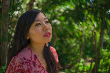 outdoors Summer lifestyle portrait of young beautiful and happy Asian Chinese woman in elegant dress walking tranquil and cheerful in green city park or wood in harmony and serenity 