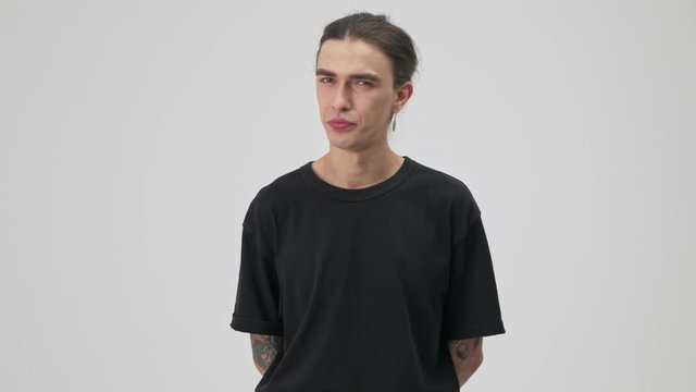 Serious young tattooed brunette man in black t-shirt disagree with someone and shaking his head negatively while looking at the camera over gray background isolated