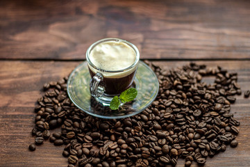 A cup of delicious, aromatic coffee. It is on a substrate of coffee beans. Has a lush, white foam. Decorated with mint leaves. 