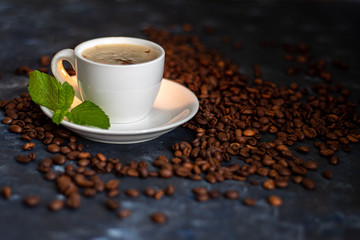 A cup of delicious, aromatic coffee. It is on a substrate of coffee beans. Has a lush, white foam. Decorated with mint leaves. 