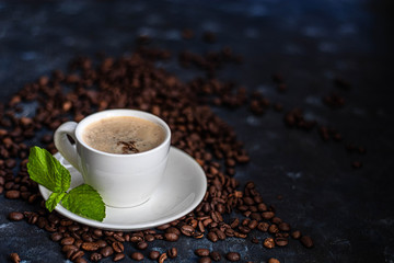 Obraz premium A cup of delicious, aromatic coffee. It is on a substrate of coffee beans. Has a lush, white foam. Decorated with mint leaves. 