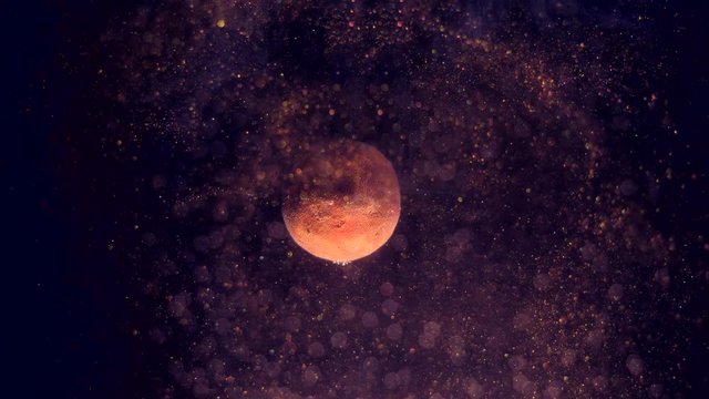 Rotation of tiny planet around its axis. Sparkling gold space dust swirling randomly and glittering. Bokeh particles on the forefront.