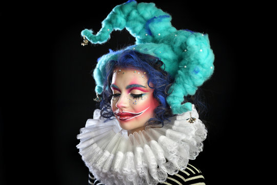 girl in makeup and costume jester . clown girl with bright makeup in blue wig On black background. eyes closed .