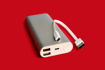 Power bank for charging mobile devices. White smart phone charger with power bank. Battery bank on a red background . External battery for mobile devices.