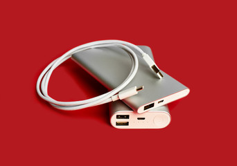 Obraz premium Power bank for charging mobile devices. White smart phone charger with power bank. Battery bank on a red background . External battery for mobile devices.