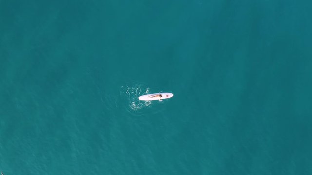 Ragazza con costume arancione va sulla tavola da surf in mare. Vista aerea con drone.