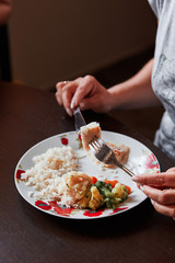 Closeup of the meal on plates on table and hands holding cutlery. People having a dinner at home. Real people, authentic situations