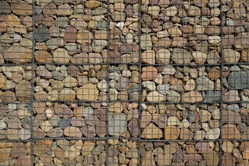 Background wall made of round colorful stones secured with steel grid.