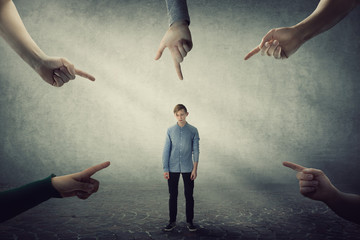 Stressed teen boy, under pressure, looking down feel ashamed and discomfort as lots of hands...