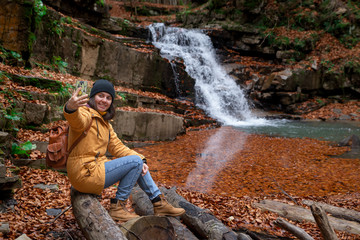 woman sitting on the log looking at waterfall autumn season