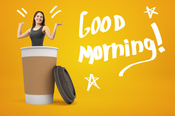 Young smiling girl popping out of big paper cup on amber background with title Good morning 