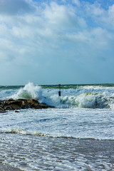 Crashing waves on a stony groyne (breakwater) during a massive storm under a majestic blue sky and white clouds