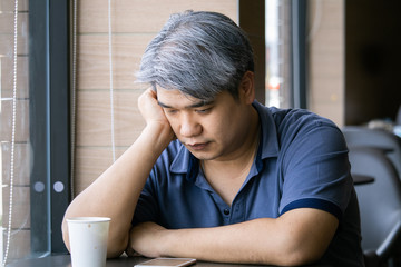 Stressed tired young Asian middle-aged man,old man take hand on head feeling depression and exhausted sitting by the window at coffee shop,grey hair man ,
