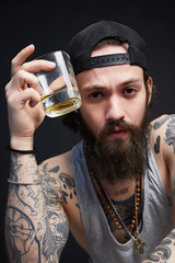 tattooed man in hat drinking a whiskey