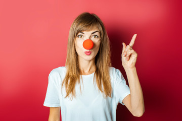 Funny young woman with a red nose of a clown on a pink background. Concept red nose day, holiday,...
