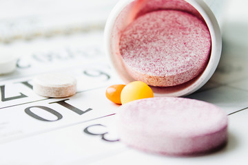 Obraz na płótnie Canvas Large pink pills or vitamins near a jar on a calendar background.