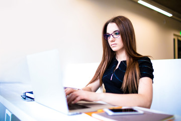 Woman marketing specialist working in internet via laptop computer, sitting in modern office space. Female experienced freelancer using applications on notebook. Entrepreneur keyboarding on netbook