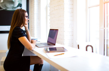 Naklejka premium Business woman talking via mobile phone after work on laptop computer. Female copywriter having cellphone conversation, sitting with netbook in coworking space. Content manager phoning via telephone