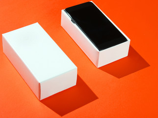 New smartphone in open box on orange paper background. Side view, minimalism