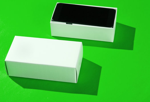 New smartphone in open box on green paper background. Side view, minimalism