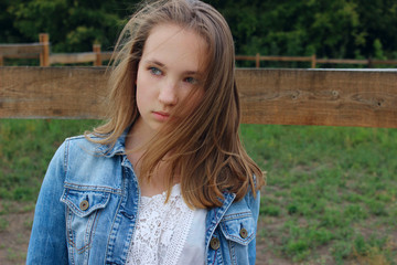 Cropped portrait of a girl in a denim jacket with developing hair. Caucasian teenage girl looking to the side outdoor, close up. Portrait of a carefree young woman with her hair blowing in the wind.