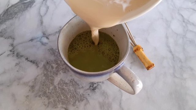 Pouring milk in matcha tea powder dissolved in water. Home made morning matcha latte