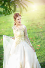Fototapeta premium Beautiful portraits with natural light asian woman bride in wedding dress in nature meadow flower,standing in green grassy field in background.