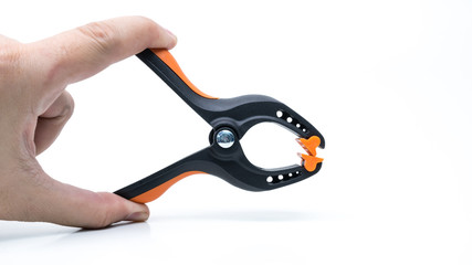 Hand holding black and orange color heavy duty plastic spring clamp. Holder or grip equipment for photography and woodworking tools. Isolated on white. Copy space.