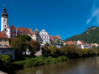 Fototapeta na wymiar Flusseitige Silouhette von Frohnleiten an der Mur im Bezirk Graz, Österreich mit blauem Himmel, Kirche und historischen Häusern